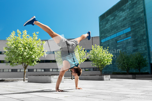 Image of young man exercising and doing handstand outdoors