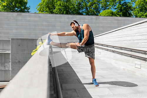 Image of young man in headphones stretching leg outdoors