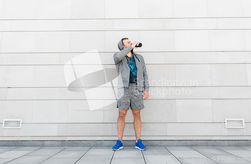Image of sportsman with bottle drinking water in city