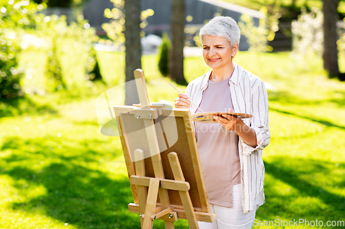 Image of senior woman with easel painting outdoors