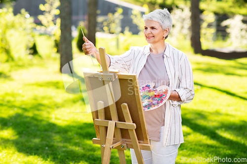 Image of senior woman with easel painting outdoors