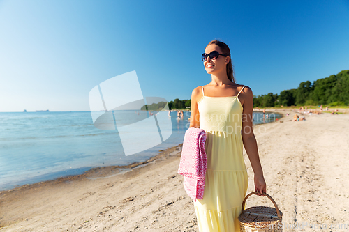 Image of happy woman with picnic basket walking along beach