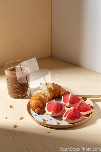 Image of glass of coffee, croissant and grapefruit on table