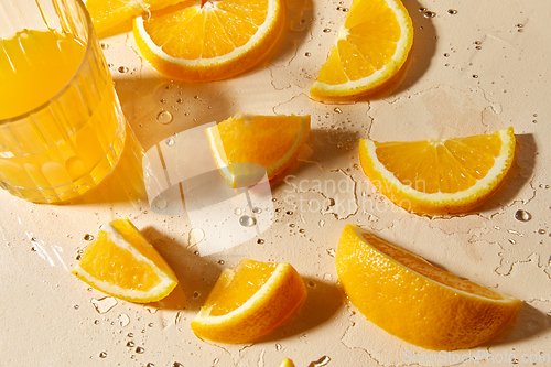 Image of glass of juice and orange slices on wet table