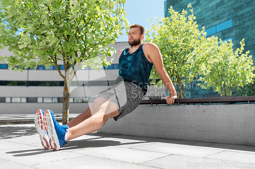 Image of young man doing triceps dip on city street