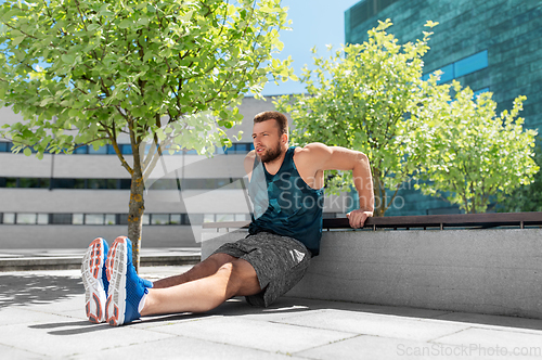 Image of young man doing triceps dip on city street