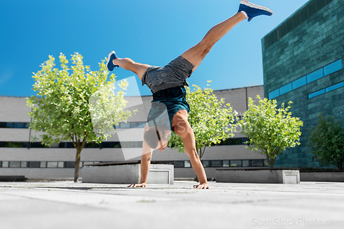 Image of young man exercising and doing handstand outdoors