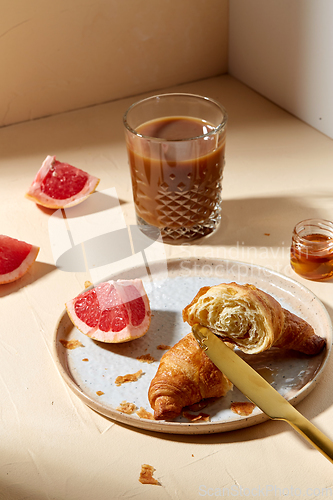 Image of glass of coffee, croissant and grapefruit on table