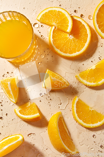 Image of glass of juice and orange slices on wet table