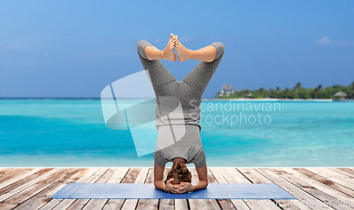 Image of woman making yoga in headstand over ocean