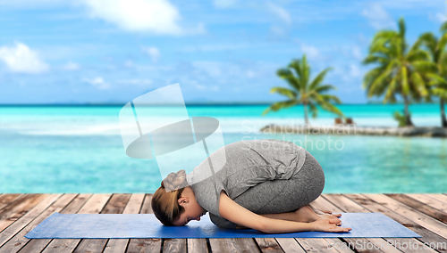 Image of woman doing yoga child pose on mat over ocean