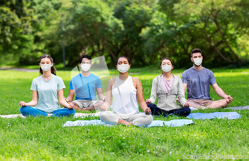 Image of group of happy people in masks doing yoga at park