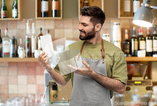 Image of happy smiling barman in apron with bill at bar