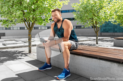 Image of happy sportsman with bottle sitting on city bench