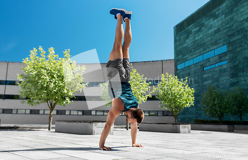 Image of young man exercising and doing handstand outdoors