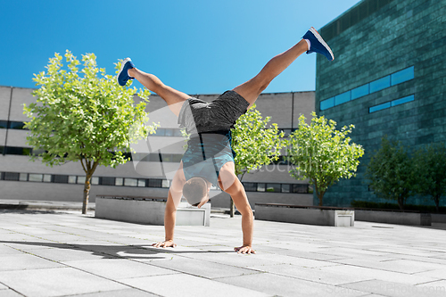 Image of young man exercising and doing handstand outdoors