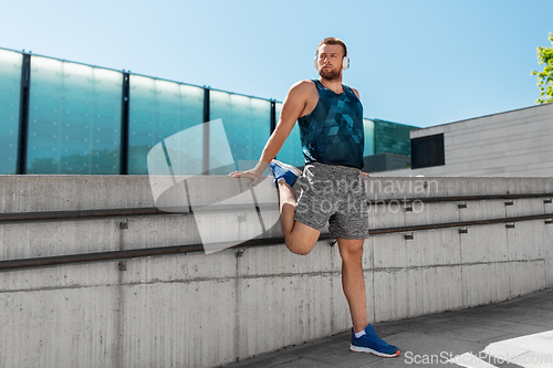 Image of young man in headphones stretching leg outdoors