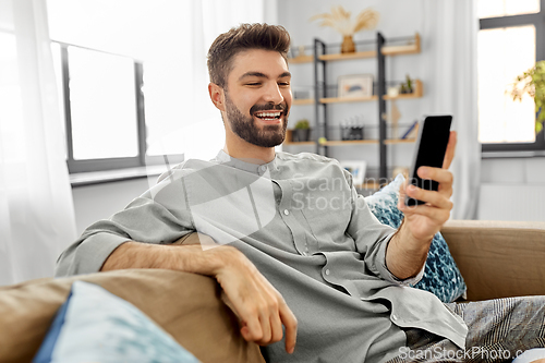 Image of happy smiling young man with smartphone at home