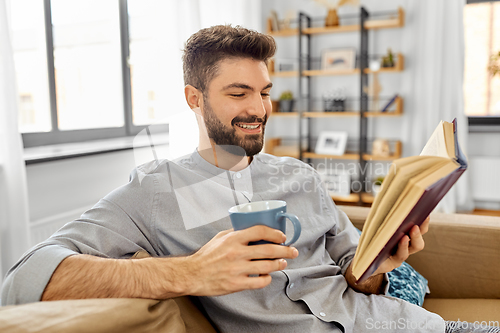 Image of man reading book and drinking coffee at home