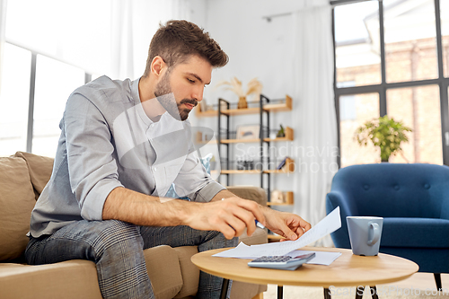 Image of man with bills counting on calculator at home