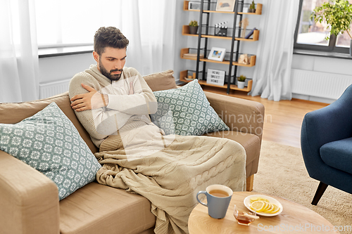 Image of sick young man in blanket drinking hot tea at home