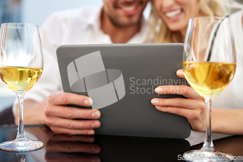 Image of happy couple with tablet pc and wine at restaurant