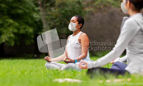 Image of group of people in masks doing yoga at summer park