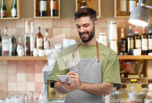 Image of smiling waiter in apron taking notes to notepad