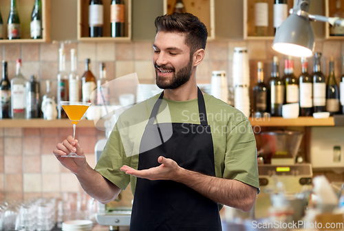 Image of happy barman in apron with glass of cocktail