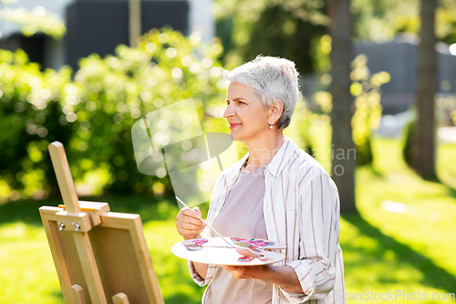 Image of senior woman with easel painting outdoors