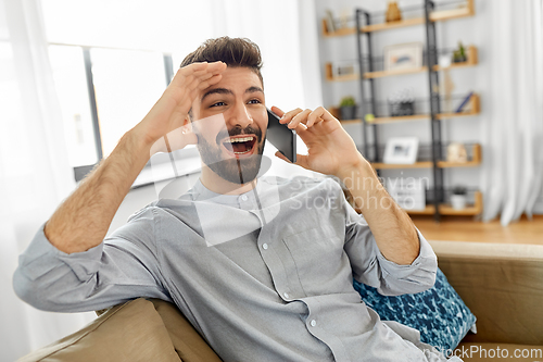 Image of happy man calling on smartphone at home