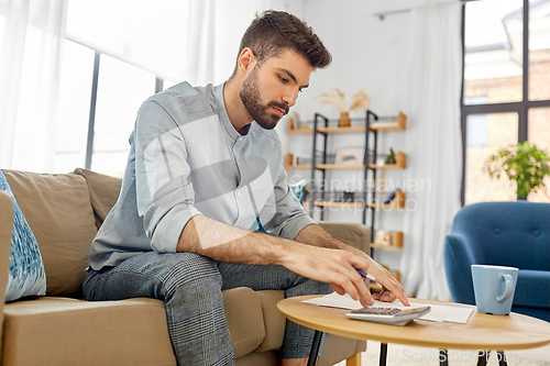 Image of man with bills counting on calculator at home