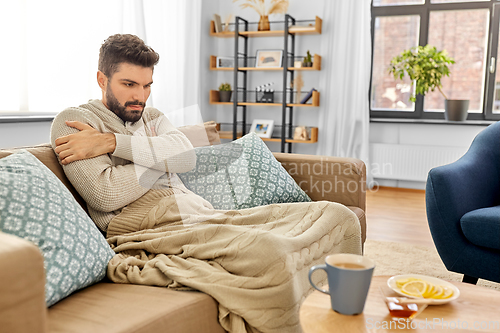 Image of sick young man in blanket drinking hot tea at home