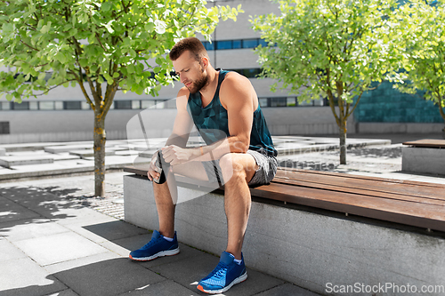 Image of tired sportsman with bottle sitting on city bench