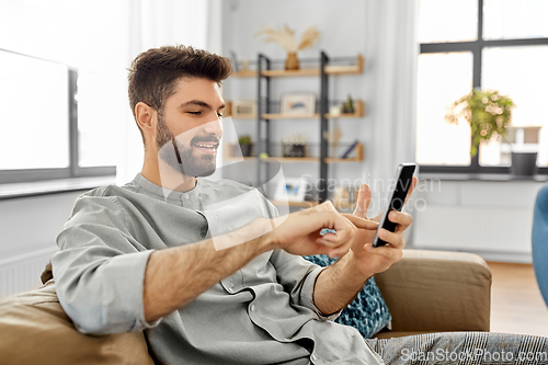Image of happy smiling young man with smartphone at home