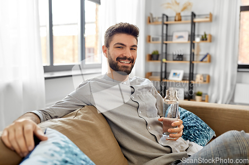 Image of happy man drinking water from glass bottle at home