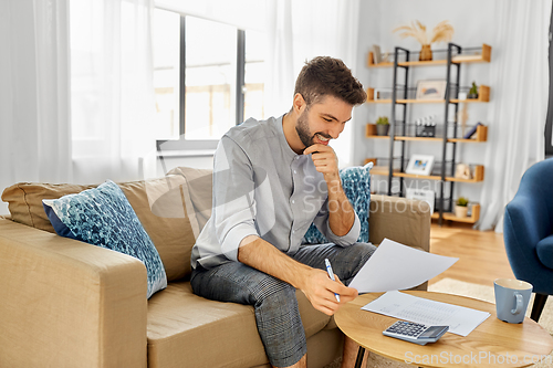 Image of man with bills counting on calculator at home