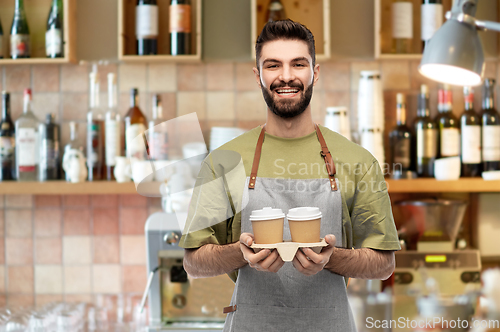 Image of happy smiling barman in apron with takeaway coffee