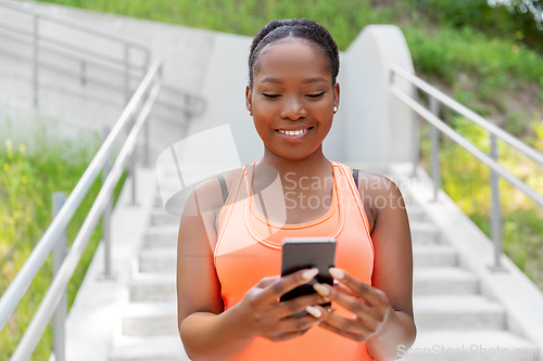 Image of smiling sporty african woman using smartphone