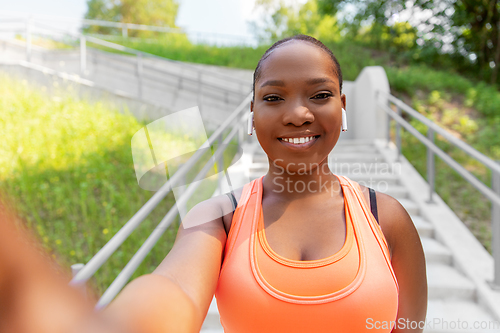 Image of happy african woman with earphones taking selfie