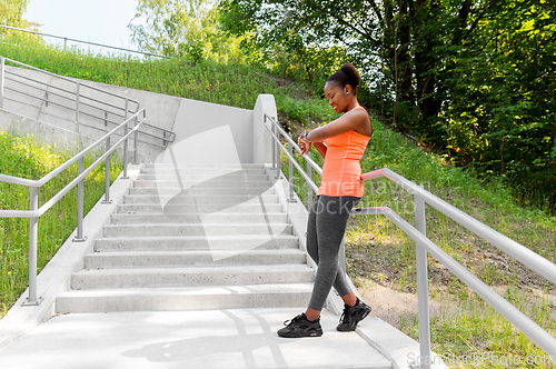 Image of happy african woman with fitness tracker outdoors