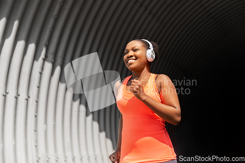 Image of happy african woman in headphones running outdoors