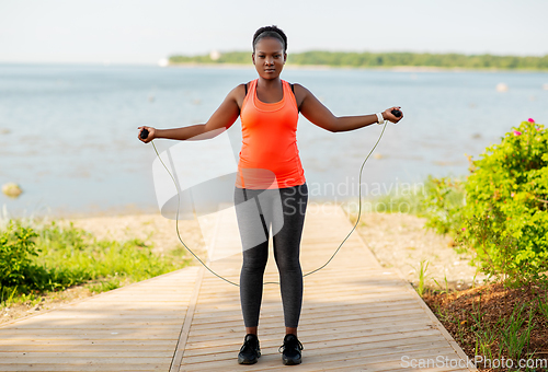 Image of african woman exercising with jump rope on beach