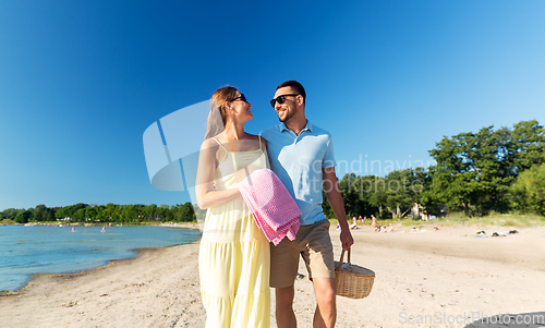 Image of happy couple with picnic basket walking on beach