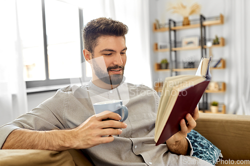 Image of man reading book and drinking coffee at home
