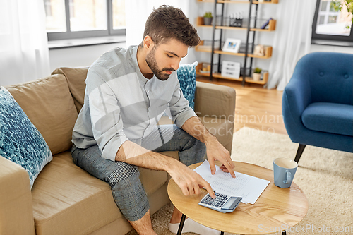 Image of man with bills counting on calculator at home