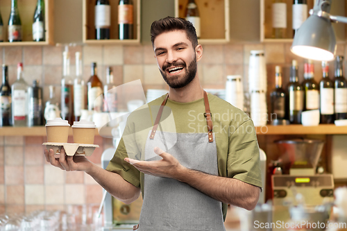 Image of happy smiling barman in apron with takeaway coffee