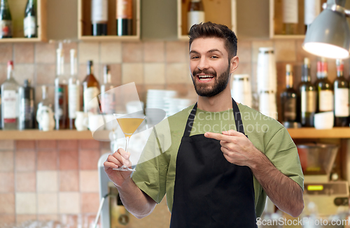 Image of barman in apron with glass of cocktail at bar