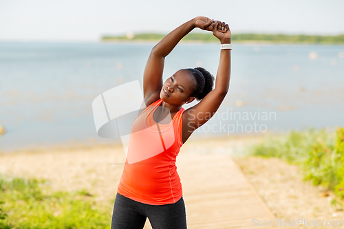 Image of young african american woman stretching outdoors