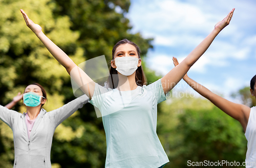 Image of group of women in masks doing yoga at summer park